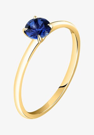 Guldring med en glat skæft, der har en oval safir holdt af seks klør, der viser en dyb blå farve og reflekterende facetter.
