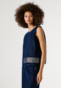 Tumesinine ilma varrukateta tops tekstureeritud kangast, millel on metallikhall vöökoht. Lihtne disain sirge lõike ja ümmarguse kaelusega.