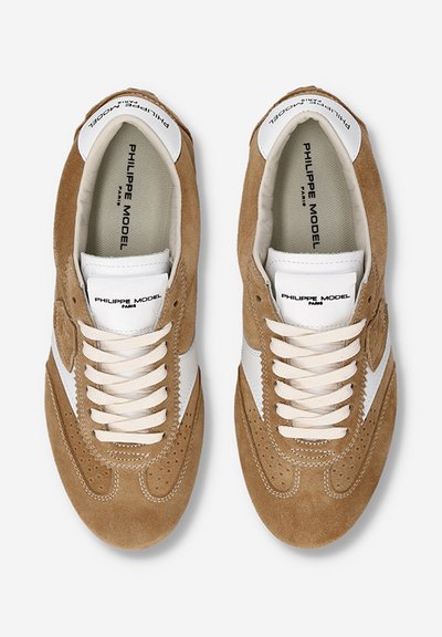 Baskets en daim marron avec un swoosh en cuir blanc, des lacets beiges, des détails perforés et un logo sur une languette rembourrée.