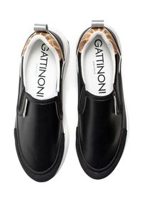 Svarta slip-on skor med en slät läderövre del, vit gummisula och mönstrad tygfoder. Har en bakre dragflik.