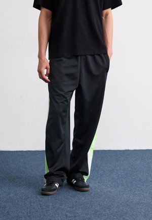Svarta idrottsbyxor med gröna sidodetaljer, tillverkade av ett smidigt material. Löst skuren med resår i midjan. Styla med en svart t-shirt och sneakers.