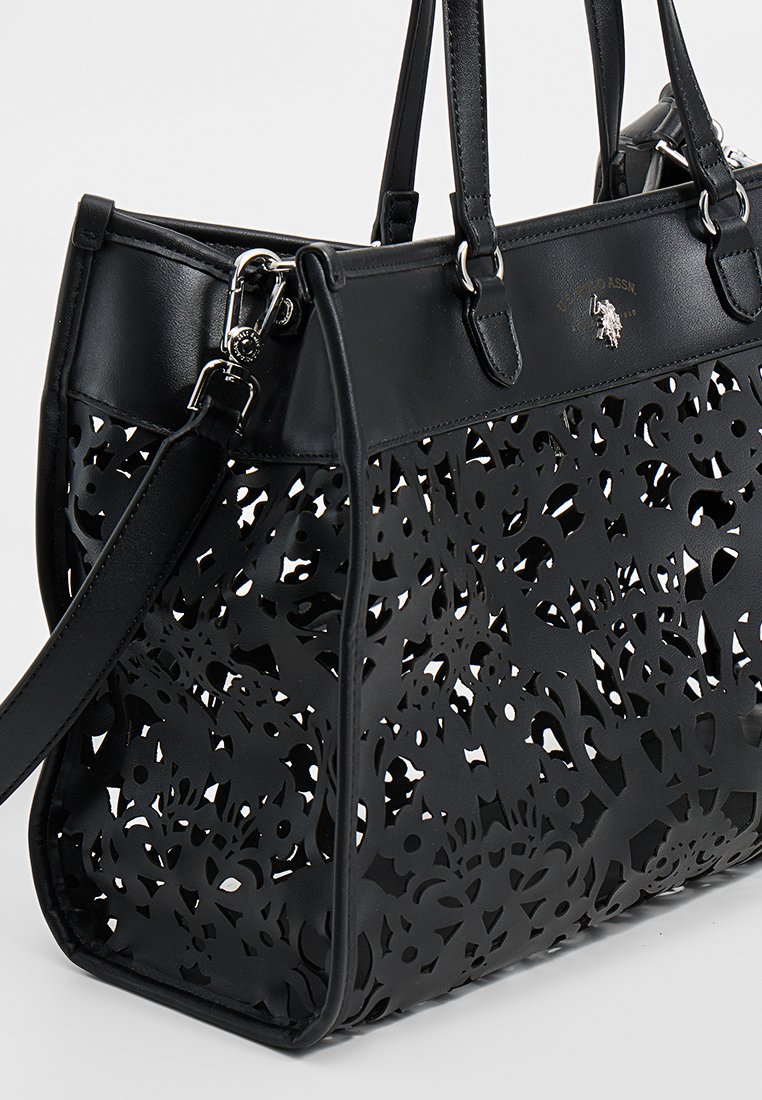 Bolso de mano negro con un diseño de flores recortadas, hecho de material sintético. Cuenta con dos asas, una correa desmontable y herrajes en tono plateado.