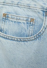 Tessuto in denim azzurro chiaro con una tasca posteriore con cuciture visibili e sottili variazioni di consistenza. Include un piccolo orlo rinforzato.