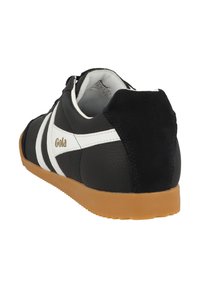 Sneaker nera con strisce bianche, realizzata in pelle testurizzata e suede, con una suola in gomma beige e il marchio "Gola" sul lato.