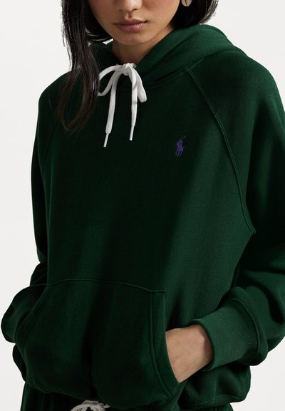 Donkergroen hoodie van zachte stof, met een voorkangoek, witte trekkoorden en een klein paars logo op de borst.