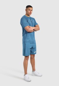 Camiseta atlética azul con cuello redondo y mangas cortas, combinada con pantalones cortos azules. Zapatillas blancas de diseño simple, material ligero.