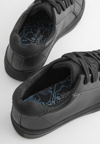 Baskets noires avec un extérieur en cuir lisse, un talon texturé et des semelles intérieures à motifs bleus présentant des dessins en forme de circuits.