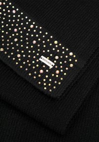 Černá pletená látka s texturovaným vzorem, zdobená mnohobarevnými kamínky uspořádanými do dekorativního designu a malým štítkem značky WITTCHEN.