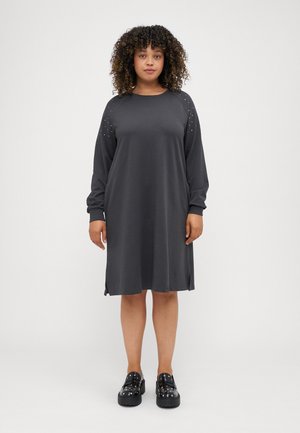 Abito grigio a maniche lunghe con spacchi laterali, caratterizzato da accessori con borchie sulle spalle. Tessuto morbido, vestibilità rilassata, design fino al ginocchio. Scarpe con plateau nere.