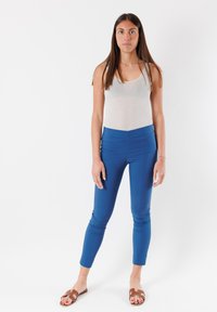 Leggings azzurrini a vita alta realizzati in tessuto elastico, abbinati a una canotta grigia chiara e sandali marroni a scivolo. Design semplice e aderente.