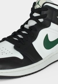 Ασπρόμαυρο παπούτσι Nike Air Jordan με πράσινο λογότυπο Nike και μαύρα κορδόνια, εμφανιζόμενο σε κοντινή λήψη από την εμπρόσθια πλευρά.