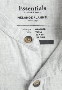 Hele hallikas särk, mis on valmistatud 100% puuvillast, melange flanelltekstuuriga, nööbiga kinnitamine ja brändi sildiga detailid.