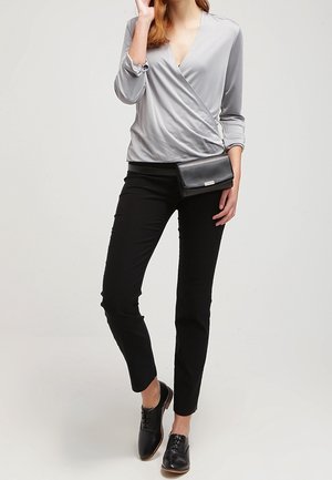 Blouse grise à manches longues, pantalon slim noir, chaussures noires à lacets, accompagnés d'une pochette noire.
