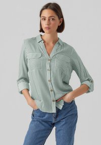 Light green striped button-up shirt with two chest pockets, rolled sleeves, and wooden buttons. Soft fabric with a relaxed fit.