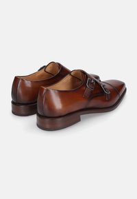 Braune Lederschuhe mit glatter Oberfläche, spitzen Zehen, zwei Schnallen und einem gestapelten Holzabsatz. Leicht gewölbte Form hinten.