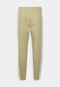 Beige sweatpants gjorda av bomull, med vita sidostrepor och en tryckt logotyp på underbenet. Resårmidja och smal passform.