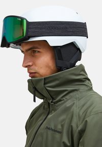 Witte skihlem met zwarte band met het label "ATOMIC" en groen spiegelende skibril. Olijfgroene waterdichte jas met zwarte rits en logo.