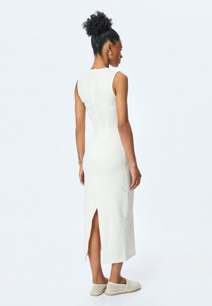 Witte, mouwloze jurk met een gestructureerd patroon, taps toelopende vorm, een split aan de achterkant en een zichtbare rits. Gecombineerd met lichte, geweven instap schoenen.