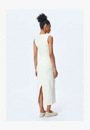Vestido blanco sin mangas con un patrón texturizado, forma ajustada, abertura en la parte trasera y una cremallera visible. Combinado con zapatos ligeros y de tejido tipo slip-on.