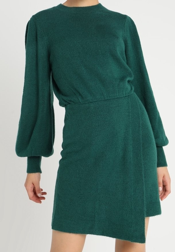 Robe en maille verte avec un col rond, des manches longues bouffantes, une taille cintrée et un ourlet asymétrique. Texture douce et coupe décontractée.