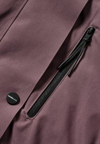 Bordowy materiał o gładkiej teksturze posiada zasuwaną kieszeń obszytą na czarno, ozdobioną okrągłym czarnym guzikiem z napisem "FUTURESENSE."