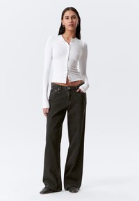 Chemise blanche à manches longues et à boutons associée à un jean large noir. La chemise présente un design ajusté et une texture douce ; le jean a une coupe décontractée.