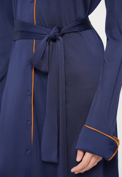 Φόρεμα σε ναυτικό μπλε με κουμπιά και ζώνη δεμένη στη μέση, με πορτοκαλί διακοσμητικές ραφές στα μανίκια και στο εμπρόσθιο μέρος, κατασκευασμένο από υφή ύφασμα.