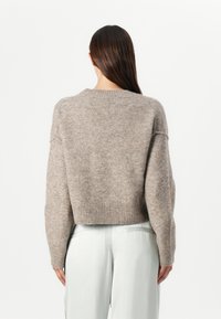 Brun ullblandet cropped genser med ribbestrikket nederkant, senkede skuldre og myk tekstur. Modellen har på seg lyse bukser.