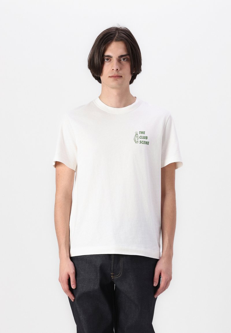 Hvid bomulds t-shirt med korte ærmer. Har et grønt grafisk print på venstre bryst med teksten "THE CLUB SCENE." Enkel design, rund hals.