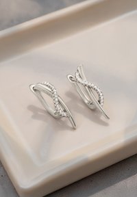 Srebrne kolczyki o skręconym wzorze, z rzędem małych, przezroczystych kamieni po jednej stronie. Gładka powierzchnia, błyszczące wykończenie.