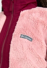 Fleecejakke i blød pink med en bordeaux inderside. Har en lynlås og et gråt Columbia-logo patch på venstre side.