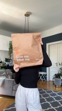 Busta di carta marrone con testo "Amami. Indossami." e logo Zalando. Tenuta davanti al viso, che mostra una superficie texturizzata e sgualcita.