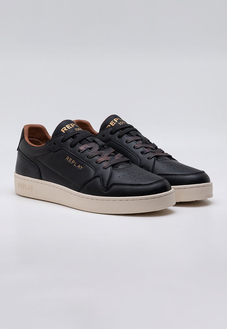 Zwarte leren sneakers met geperforeerd ontwerp, beige rubberen zool, bruine accenten, en reliëf 'REPLAY' logo aan de zijkant.