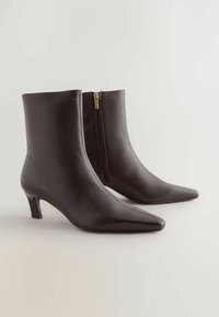 Czarne skórzane botki za kostkę z wąskim noskiem, średniej wysokości obcasem blokowym i zapinaniem na zamek z boku. Gładka tekstura i elegancki design.