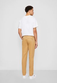 Chinos beiges avec une texture lisse et une coupe droite, associés à un t-shirt en coton blanc. L'ensemble présente un accent logo dans le dos.