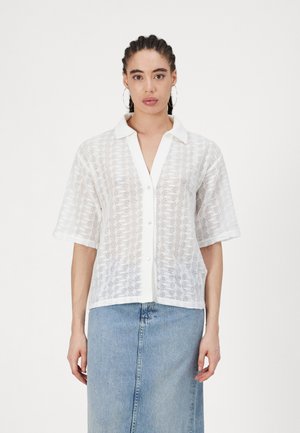 White short-sleeve shirt with a textured pattern and open collar, featuring button closure and a relaxed fit, paired with a denim skirt.