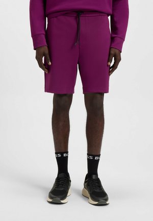 Lila elastiska shorts med dragsko i midjan, med en slät textur och en avslappnad passform. Bärs med svarta sneakers och strumpor.