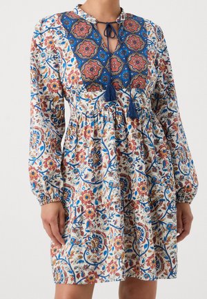 Lange mouwen jurk met bloemige en geometrische patronen in blauw, rood en oranje, voorzien van een blauwe kwastjesstrik bij de halslijn en een geplooide taille.