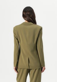 Olive green blazer with a tailored fit, notched lapels, and single back vent. Features structured shoulders and smooth fabric.
