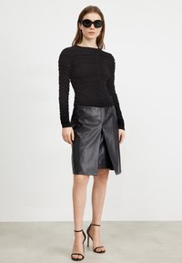Svart langermet topp med detaljer av samlet stoff, parret med et svart skinnskjørt med en frontspalte og høye sandaler.