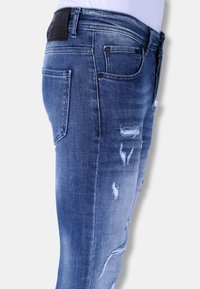 Vervaagde blauwe denim jeans met een slim fit, voorzien van versleten details en een leren label bij de tailleband. Vijf-pocket ontwerp.