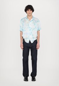 Kortærmet, lyseblå tie-dye skjorte med knaplukning i en afslappet pasform, parret med mørke denimjeans og sorte sko.