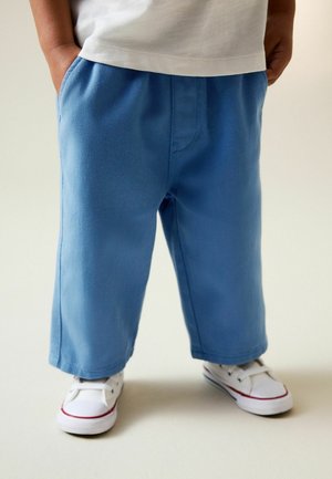 Hellblaue, weit geschnittene Hose aus strukturiertem Stoff mit Kordelzug an der Taille und Seitentaschen, kombiniert mit weißen Turnschuhen.