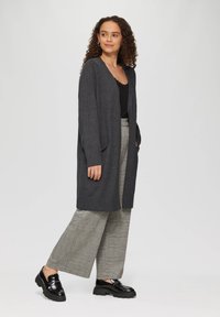 Długi szary kardigan wykonany z miękkiego plecionej tkaniny, z otwartym przodem, dwiema przednimi kieszeniami i luźnym krojem, zestawiony z szerokimi spodniami w kratę.