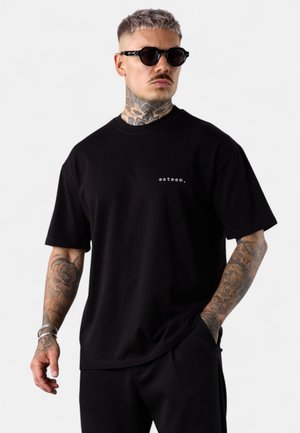 Schwarzes T-Shirt mit kurzen Ärmeln aus Baumwolle, mit einem kleinen weißen Textlogo "esteem." auf der linken Seite. Geschmeidige Textur, lockere Passform.