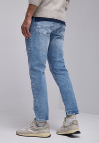 Jeans de mezclilla de color azul claro con un corte ajustado, que presentan bolsillos traseros y un desvanecimiento sutil. Combinados con zapatillas beige y un suéter de punto.