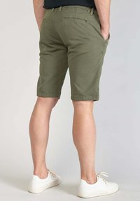 Olijfgroene shorts van lichtgewicht stof, slim fit met zijzakken, achterzak en geslagen zomen, gecombineerd met witte sneakers.