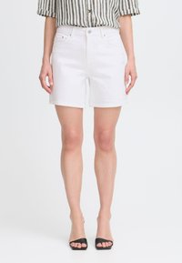 Shorts de denim blanco con cintura alta, dobladillo enrollado y dos bolsillos frontales. Combinados con una blusa a rayas en blanco y negro y tacones negros.