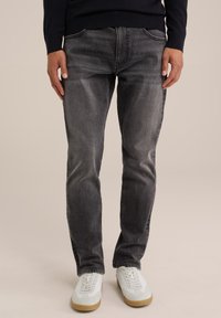 Jeans in denim grigio con una finitura sbiadita, slim fit, cinque tasche e dettagli di cucitura sottili, abbinati a sneakers bianche e un maglione blu navy.