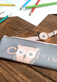Graue Stofffedertasche mit einem rosa Eulenmotiv und dem Text "Coo". Hat einen goldenen Reißverschluss und liegt auf einer Holzoberfläche zusammen mit Schreibwaren.